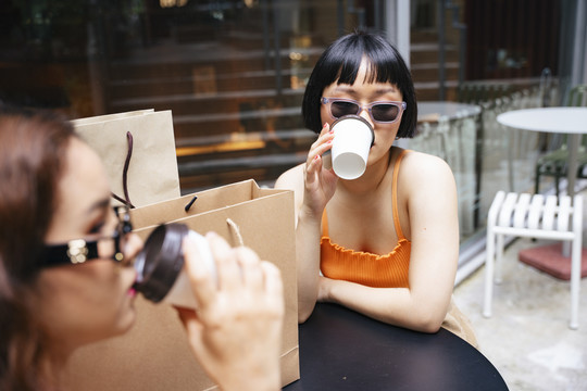 年轻的亚洲女人戴着太阳镜在咖啡馆喝咖啡的照片。