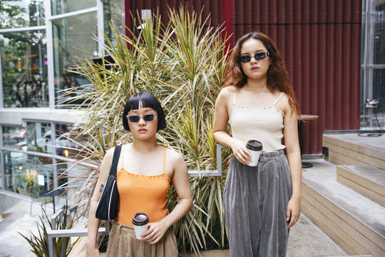 两位年轻时髦的亚洲女性手持外卖咖啡杯的肖像。