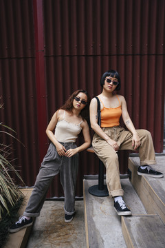 两位年轻亚洲女性在城市街道户外戴着太阳镜的时尚肖像。