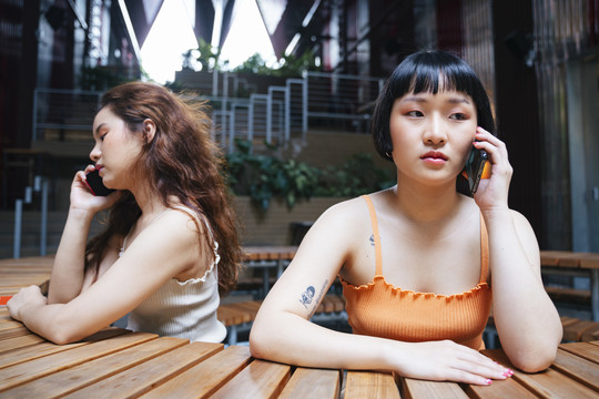 两位年轻亚洲女性分别在电话中交谈的照片。