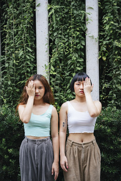 在现代公园里，两位年轻的亚洲女性的肖像覆盖了手和嘴。