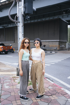 两位年轻的亚洲女性在城市街道上戴着太阳镜的时尚肖像。
