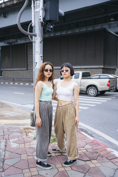 两位年轻的亚洲女性在城市街道上戴着太阳镜的时尚肖像。
