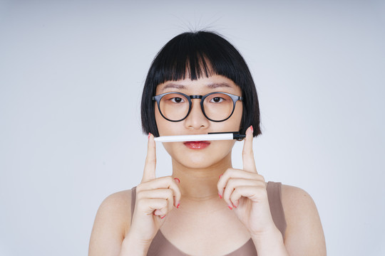 年轻亚洲女性短发的肖像，戴着墨镜，手持钢笔，白色背景。