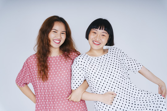两位身穿白色和粉色服装的亚洲年轻女子手挽着手跳舞的肖像。