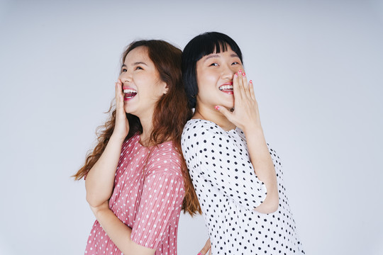 在白色背景下，两位年轻的亚洲女性在一起大笑的肖像。