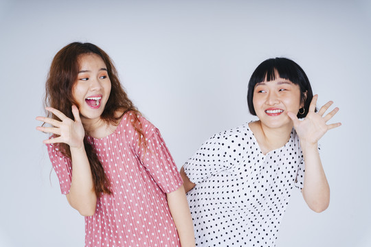 在白色背景上，两位年轻的亚洲女性穿着礼服，表达惊讶和兴奋。