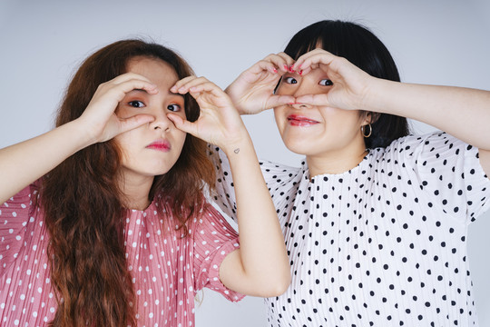 两名年轻亚洲女性在白色背景上表现双眼姿势的肖像。