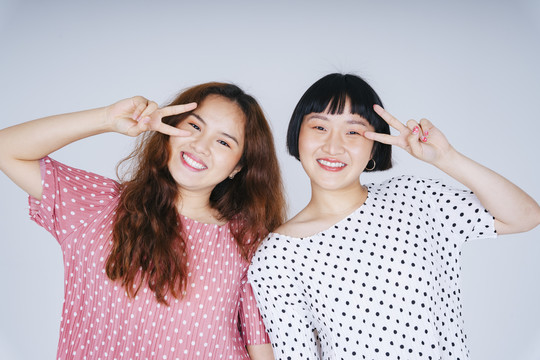 两名年轻亚洲女性的肖像，在白色背景上穿着粉色和白色的帕卡多特隔离服。