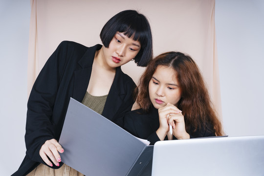 两位穿着正式夹克套装的年轻亚洲商界女性在办公室一起工作的肖像。