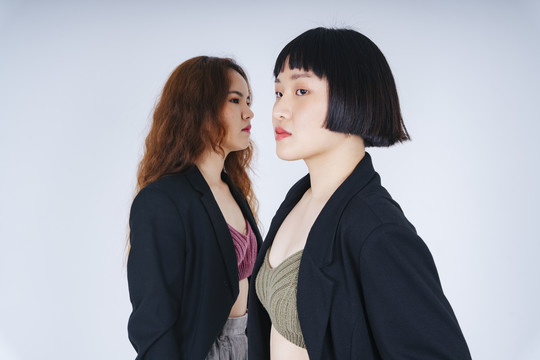 两位穿着黑色夹克套装、背景为白色的年轻亚洲商界女性的肖像。