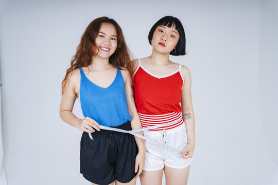 两名亚洲年轻女性的肖像，白色背景，带体重卷尺。