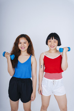 两位身穿蓝色和红色衬衫、手持哑铃的亚洲年轻女性的肖像，背景为白色。