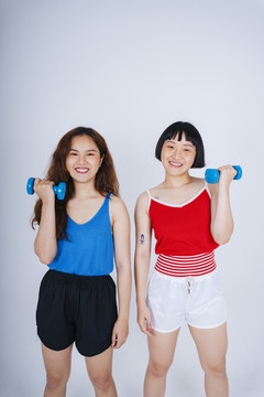 两位身穿蓝色和红色衬衫、手持哑铃的亚洲年轻女性的肖像，背景为白色。