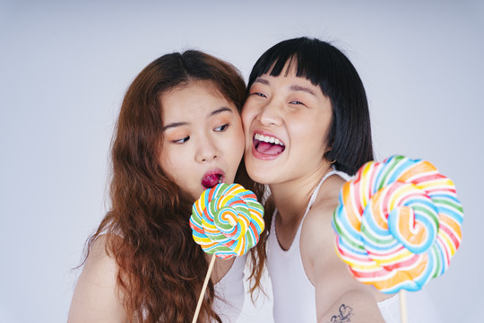 两位亚洲年轻女性的特写肖像，白色的彩虹甜棒棒糖。