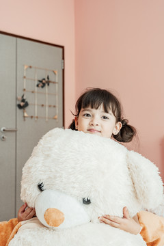 可爱的小女孩在卧室里抱着毛茸茸的大熊娃娃。