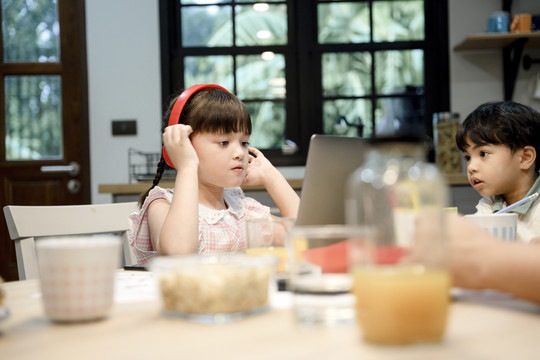 小女孩戴着耳机听音乐，看着家里的笔记本电脑。