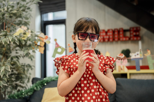 穿着红色连衣裙的小女孩在聚会上喝果汁的画像。
