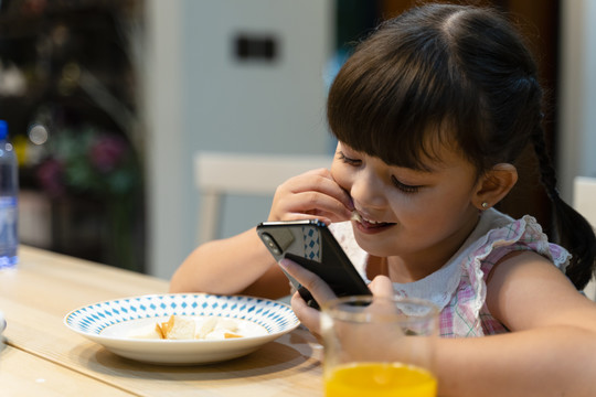 小女孩在家吃早餐和使用智能手机的特写照片。