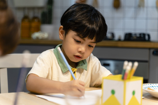 小男孩在家里厨房的桌子上做作业。