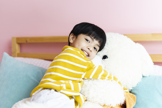 亚洲小男孩在卧室拥抱毛茸茸的大熊娃娃。
