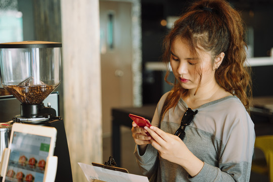 年轻女子在酒吧等待咖啡时使用智能手机。
