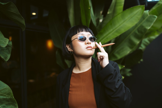 酷酷的亚洲短发女人戴着墨镜，手里拿着钢笔，像香烟一样。