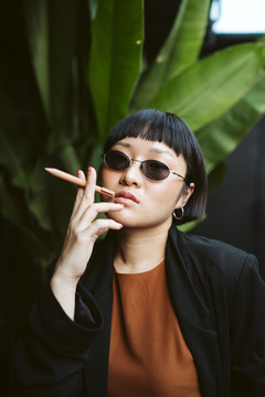 酷酷的亚洲短发女人戴着墨镜，手里拿着钢笔，像香烟一样。