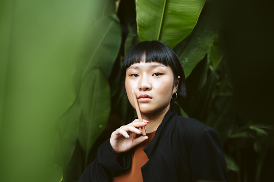 年轻的亚洲女人的肖像画短发拿着钢笔像香烟在自然界。