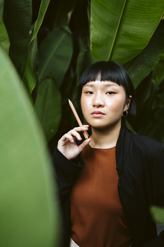年轻的亚洲女人的肖像画短发拿着钢笔像香烟在自然界。