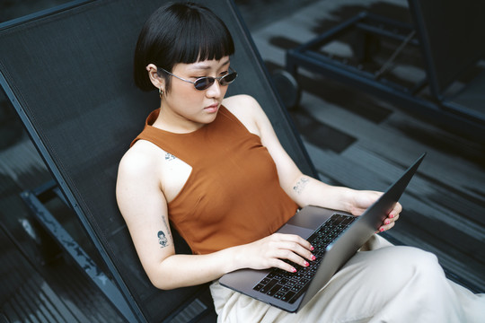 穿着休闲衬衫的女商人戴着太阳镜在创造性的工作空间与笔记本电脑一起工作。