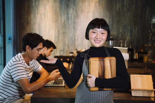 在自助餐厅拿着木制托盘的年轻亚洲短发女服务员的肖像。