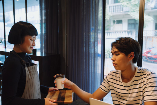 在自助餐厅为顾客提供热咖啡的亚洲女服务员。