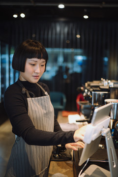 亚洲女咖啡师在咖啡馆使用数字平板电脑付账。