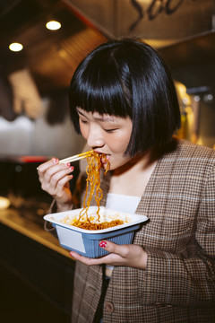 短发亚洲女人在厨房里美味地吃面条。
