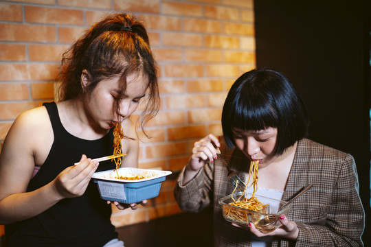 两个亚洲女人在厨房里一起吃辣面条。