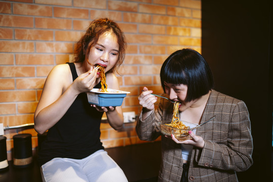 两个亚洲女人在厨房里一起吃辣面条。