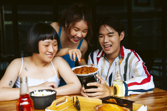 三名亚洲年轻人用智能手机在社交媒体上吃零食和看视频。