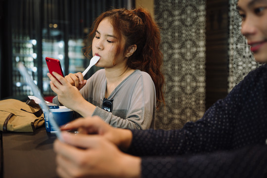 亚洲女人在咖啡馆里享受冰激凌杯和智能手机。