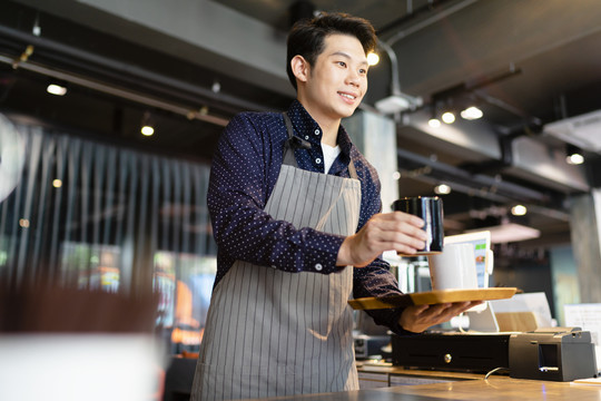 亚洲咖啡师在咖啡馆为顾客提供热咖啡。