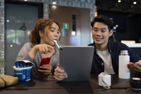 一对亚洲夫妇在咖啡吧看数码笔记本电脑。