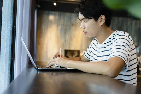 自由职业者在咖啡馆用笔记本电脑辛勤工作的侧视图。