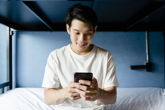 亚洲年轻人在卧室里用智能手机聊天。