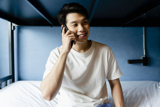 亚洲年轻人在宿舍的卧室里打电话。