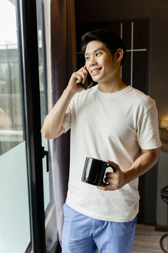 一个穿着白衬衫的亚洲人正在打电话，手里拿着一杯咖啡。