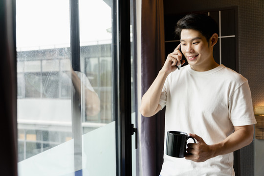 一个穿着白衬衫的亚洲人正在打电话，手里拿着一杯咖啡。