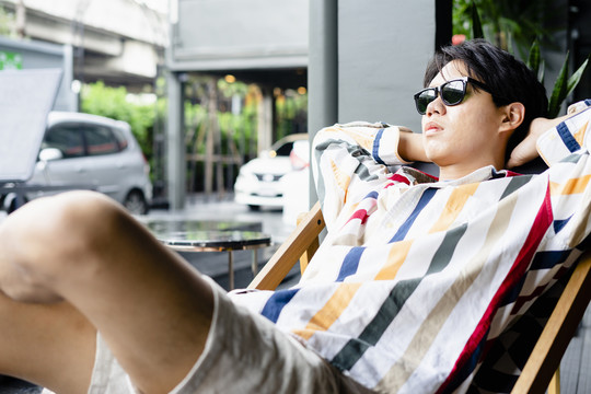戴着墨镜的亚洲年轻人在酒店的沙滩椅上放松。