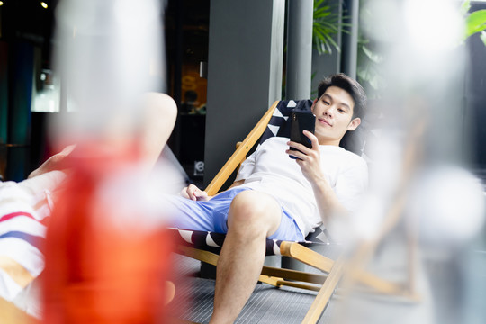 亚洲男子在酒店的沙滩椅上使用智能手机。