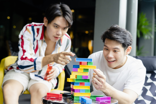 快乐的亚洲年轻人在家里一起玩jenga，和朋友们玩得很开心。