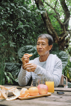 亚洲老人在户外剥橘子皮吃橘子做午餐。